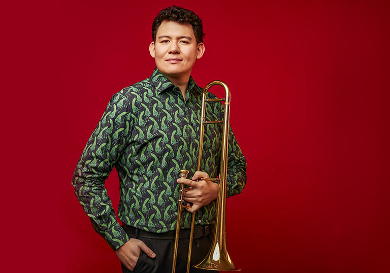 Callum Au holding trombone on red background