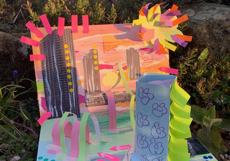 A folded piece of cardboard paper has been made into a collage of the barbican centre using cut outs of the barbican building and bright orange and blue paper