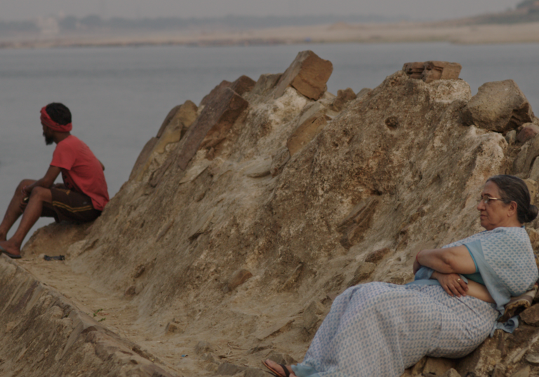 an older woman and younger man sit on a rock