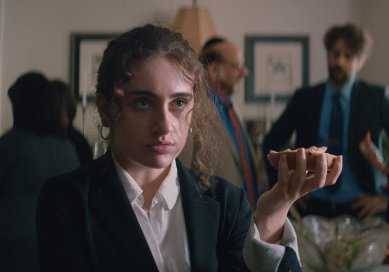 a girl stands at the wake of a funeral service with a bagel in hand