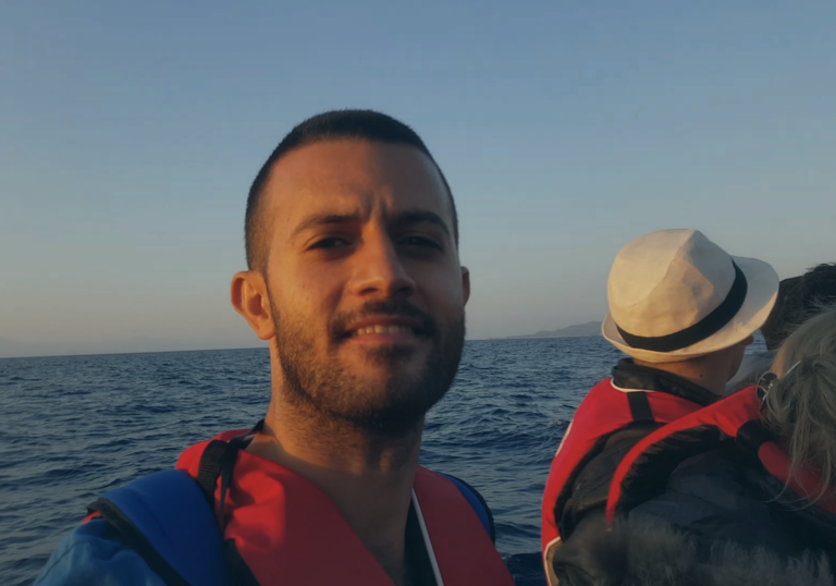 a man looks into the camera wearing a life vest and sitting on a boat