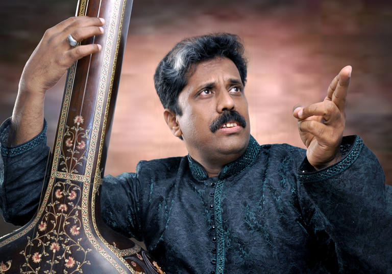 Waseem Ahmed Khan posing with his sitar, pointing to his left