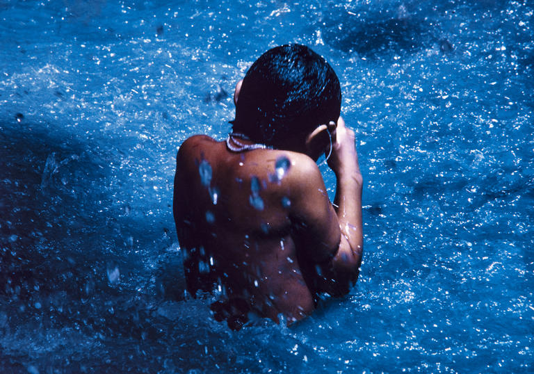 Young Yanomami boy swimming facing away from the camera