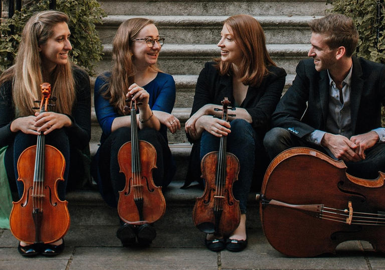Consone Quartet sitting on steps with instruments, smiling at each other