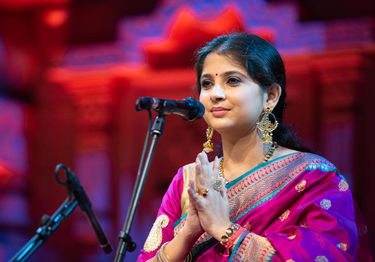 Kaushiki Chakraborty at a microphone, smiling with her hands palm together