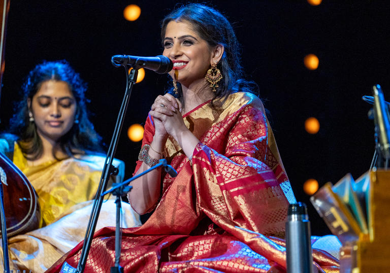 Kaushiki Chakraborty sitting at a microphone, smiling with her hands clasped together