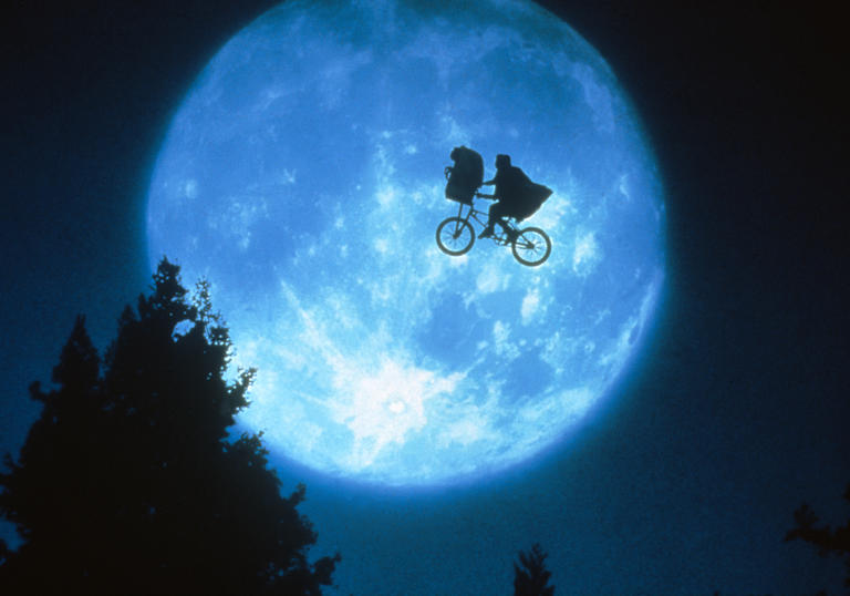 silhouette of a boy riding a bike across the moon with ET in the bike basket 