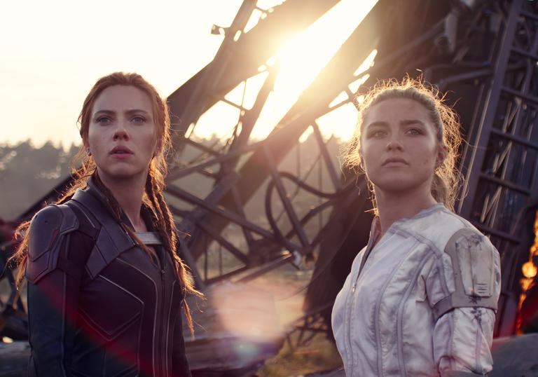 Scarlett Johansson and Florence Pugh stand together with a wreck behind them