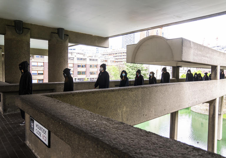a colour photo of hooded figures wearing all black walking across the Barbican highwalks