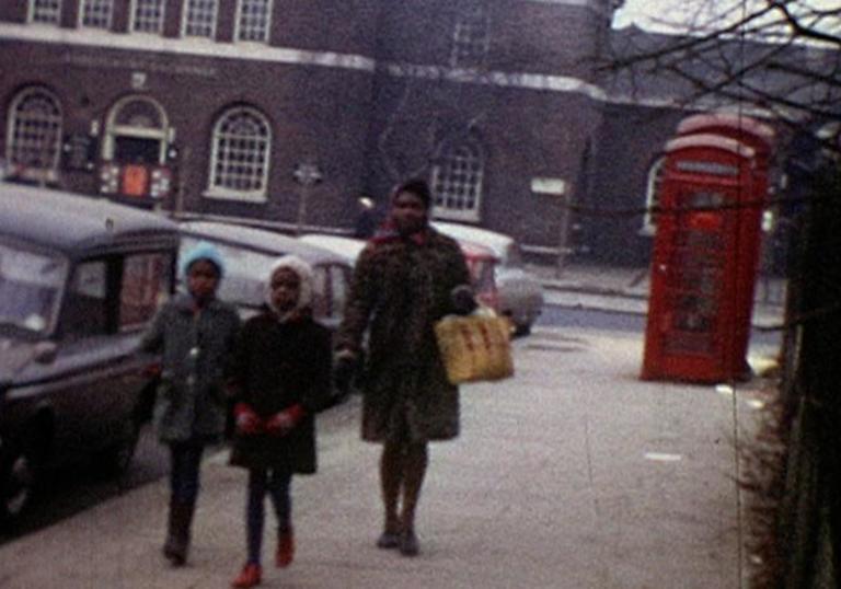 a mother and two kids walking through London with red telephone boxes in the background
