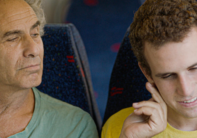 a father and his grown up son sit together on a bus