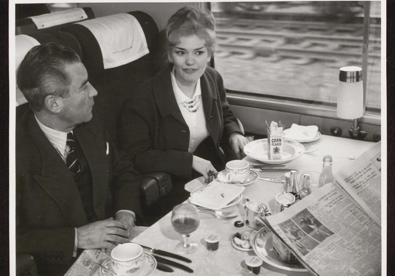 A man and a woman sit at a restaurant table in a Blue Pullman train