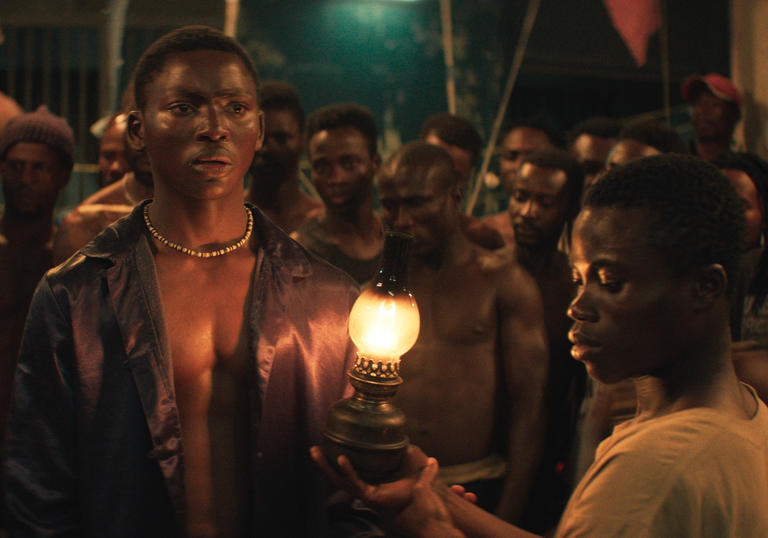 a group of men stand in a circle and a boy in the middle holds a gas lamp