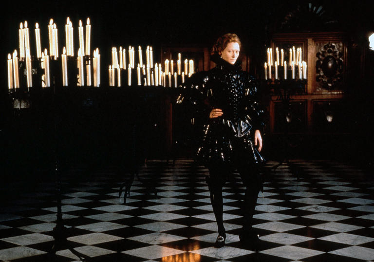 Tilda Swinton stands in a Tudor gentlemen's costume in a dimly lit room with many candles in Sally Potter's Orlando