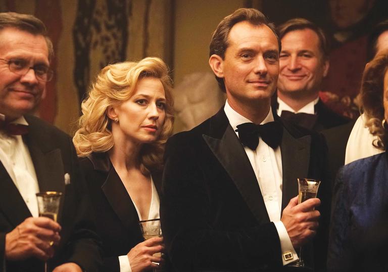Jude Law standing in a bow tie and suit holding a champagne flute in The Nest
