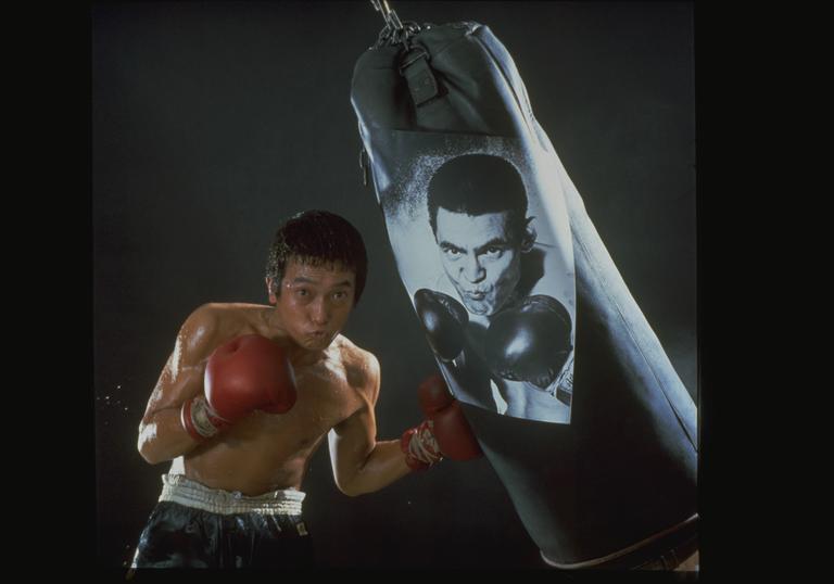 a boxer stands next to a punching bag with his boxing gloves on
