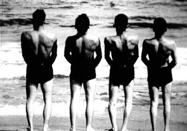 four men line up facing the sea with their backs to the camera