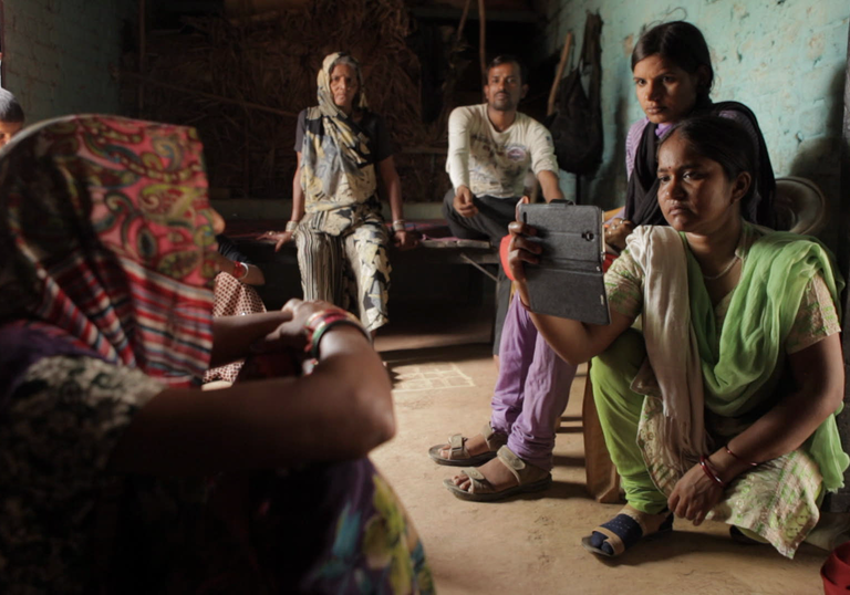 A young woman sits on the floor and holds her phone up to photograph an older woman opposite, in Writing with Fire