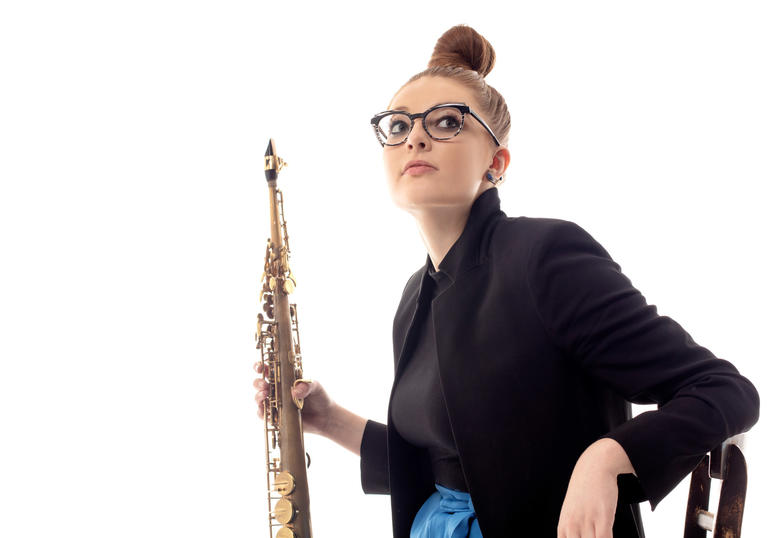 Jess Gillam sitting on a chair holding her saxophone