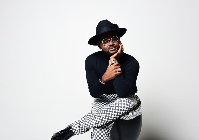 John Holiday smiling, sitting on a stool 