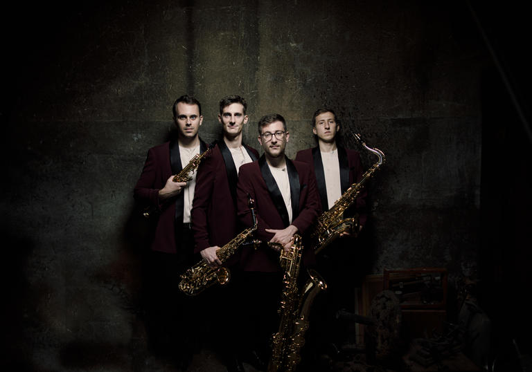 The Kebyart Ensemble stand holding their saxophones, looking at the camera