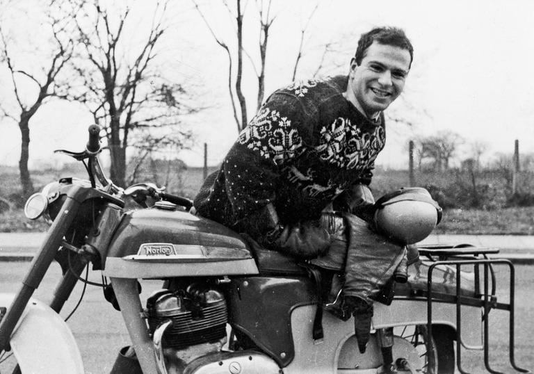 Oliver Sacks smiling at the camera holding his motorbike