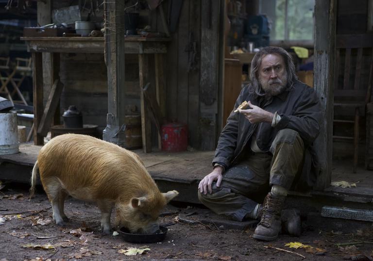 Nicholas Cage sits on the side of a dirty path with a pig next to him