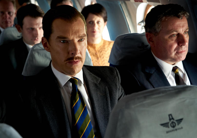Benedict Cumberbatch sits on a plan wearing a suit