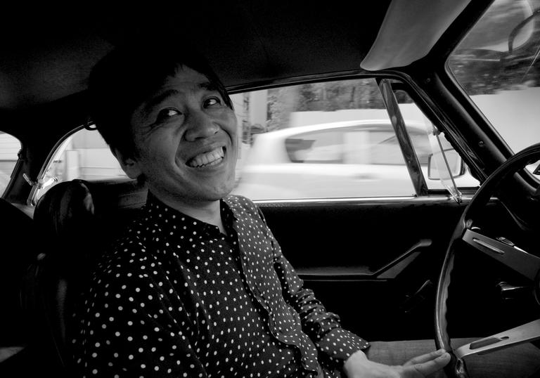 Architect Ryue Nishizawa inside his vintage Alfa Romeo car in a black and white still image 