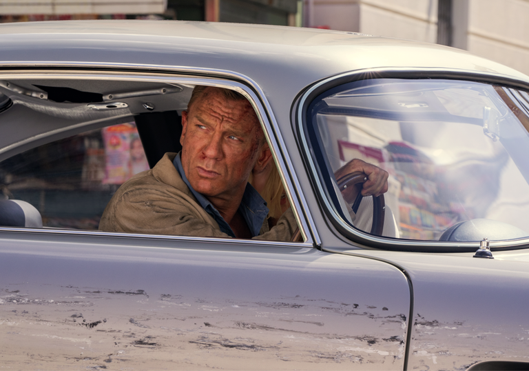 Daniel Craig as James Bond, sitting in a silver car, in a still from No Time to Die