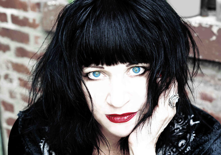 A portrait image of musician Lydia Lunch, with black hair and blue eyes