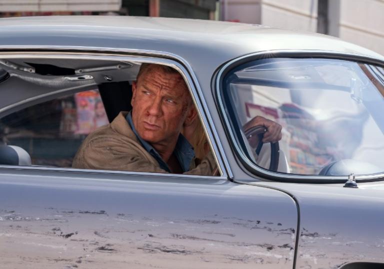Daniel Craig as James Bond, sitting in a silver car, in a still from No Time to Die