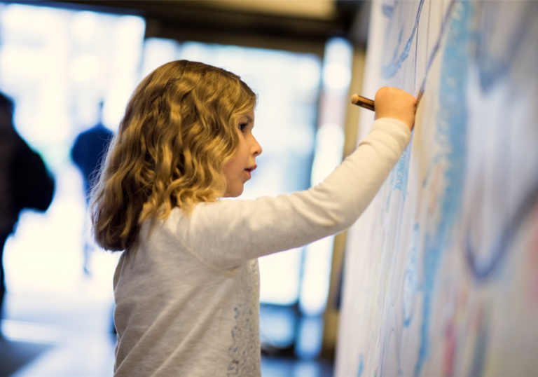A young girl draws on a wall during a workshop