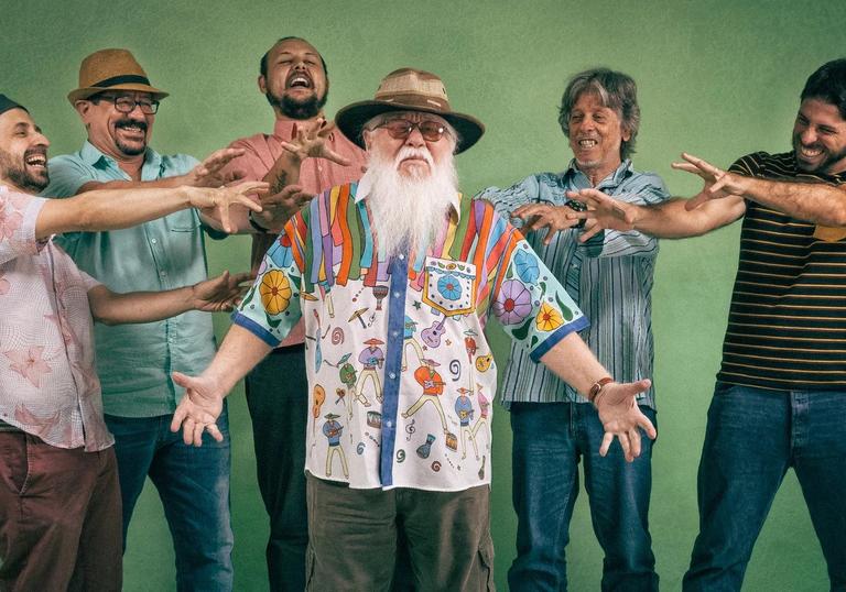 Hermeto Pascoal stands wearing a brightly coloured shirt in the centre of the photo while his bandmates point at him