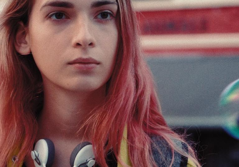 A young woman with long pink hair and earphones around her neck in the film Lola and the Sea
