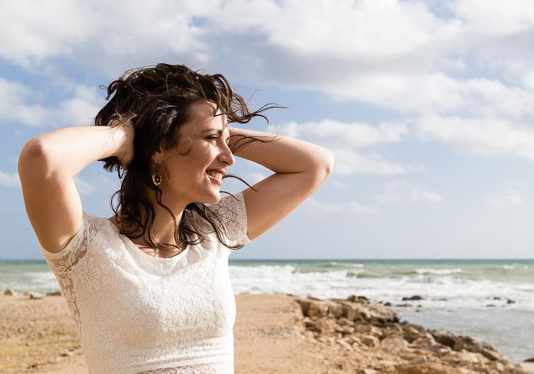 Noemi Nuti on a beach wearing a white t shirt, with both hands on her head