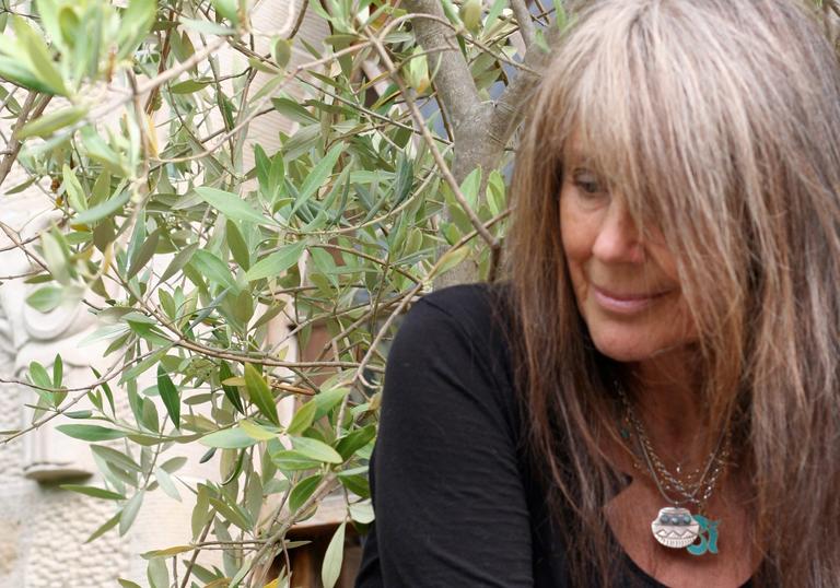 Vashti Bunyan in front of a tree, wearing a black top and long necklaces