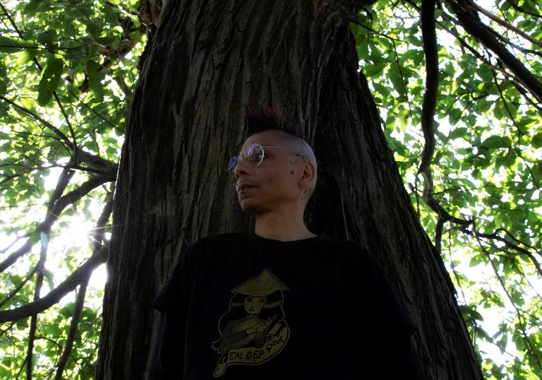 Cedrik Fermont stands in front of a large tree trunk, with the branches and leaves down either side of the image