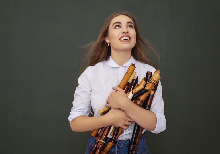 Lucie Horsch stands in the centre of the image, looking up and holding a big bundle of recorders in her arms