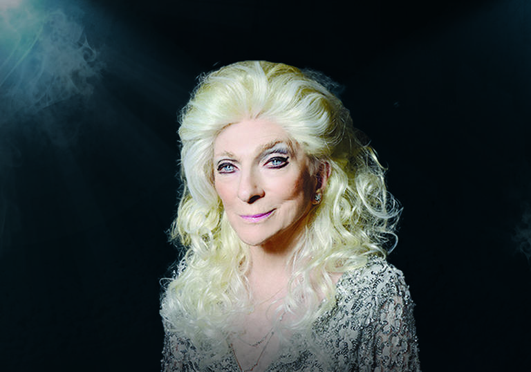 Judy Collins in front of a black background, wearing a white sequined dress