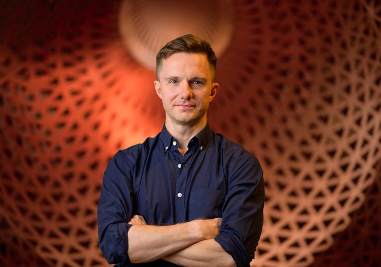 James McVinnie stands in front of a big orange dome, with his arms crossed