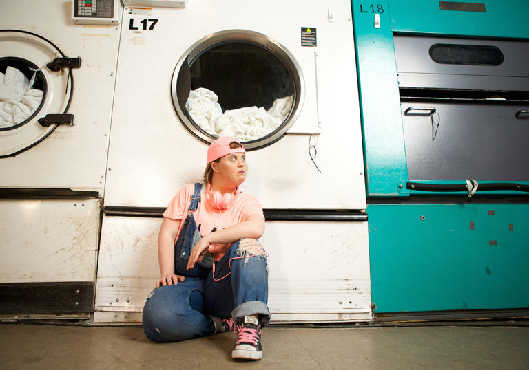 Young person wearing dungarees kneeling in front of a large washing machine