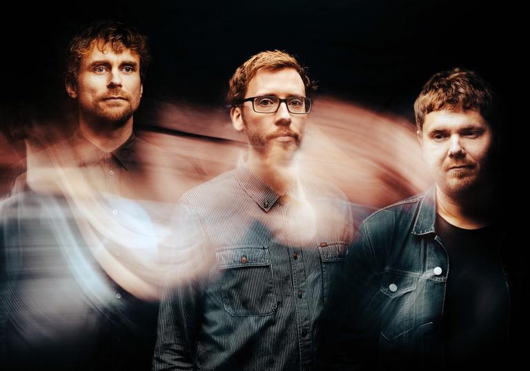 The three members of GoGo Penguin: three white men wearing denim shirts with short haircuts. There is a swirling effect over the image.