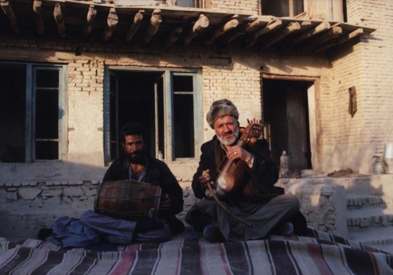 Two men sat outside playing instruments