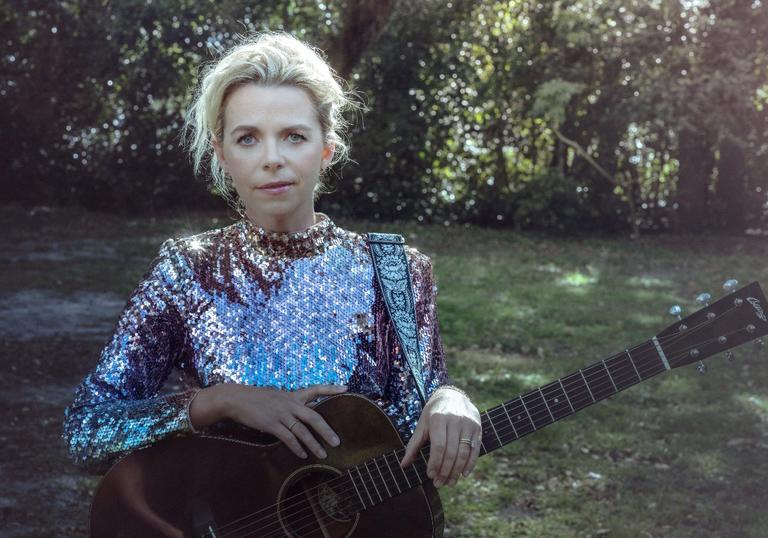 a photo of Aoife O'Donovan wearing a sequin top in a park with a guitar