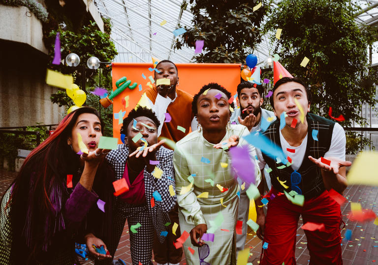 The PappyShow performers blow multi coloured confetti through the air towards the camera. 