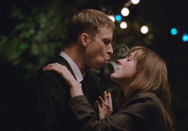 A young couple blow cigarette smoke into one another's mouths