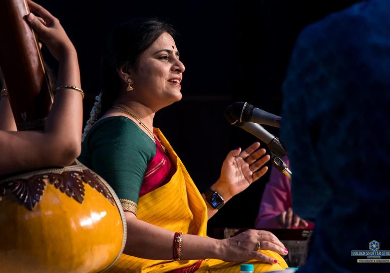 Bharathi Prathap singing, sitting cross-legged and wearing colourful clothes