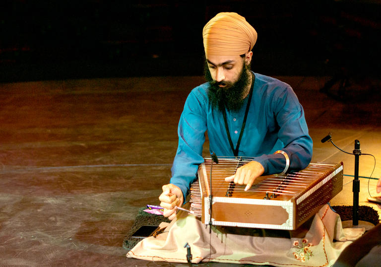 Eeshar Singh playing the santoor - a flat stringed instrument. He is wearing a beige turban and blue shirt.