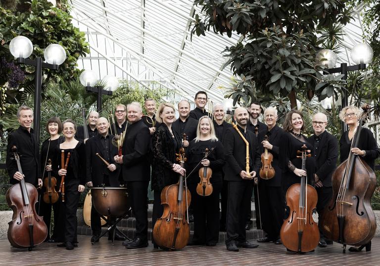Players of the Academy of Ancient Music standing with their instruments in the Barbican Conservatory